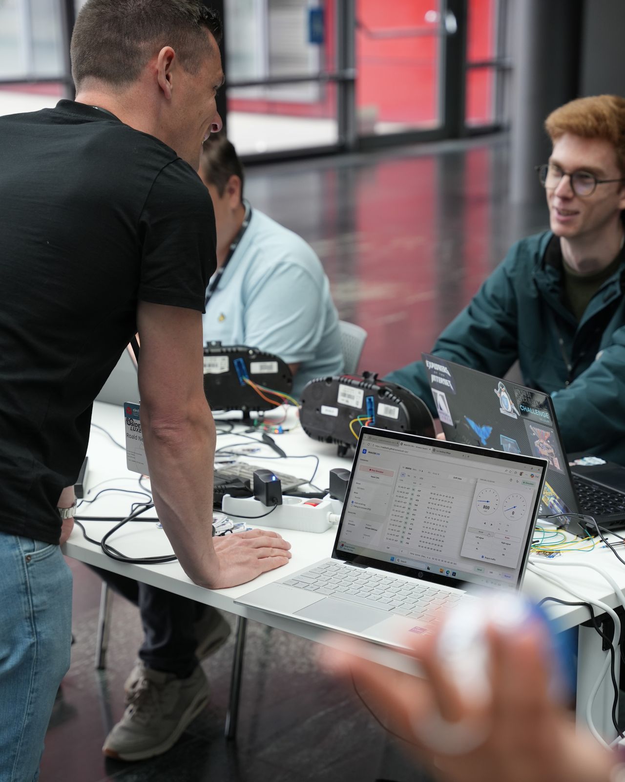 Attendees gathered around the Car Hacking Village booth, instrument clusters and laptops spread across a workshop table.
